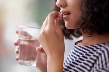 Close-up of a woman's hands and face with a glass of water while taking medication